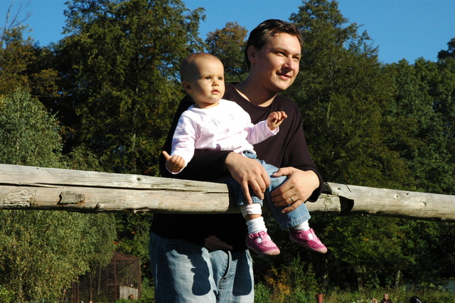 otec s dítětem sedícím na dřevěné ohradě